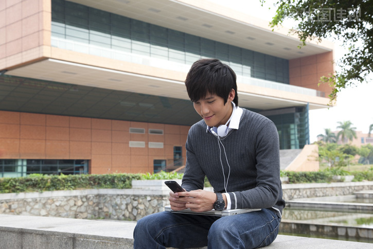 年轻男大学生在校园里使用笔记本电脑听音乐