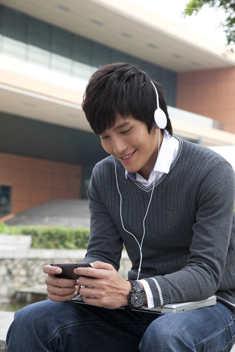 年轻男大学生在校园里使用笔记本电脑听音乐